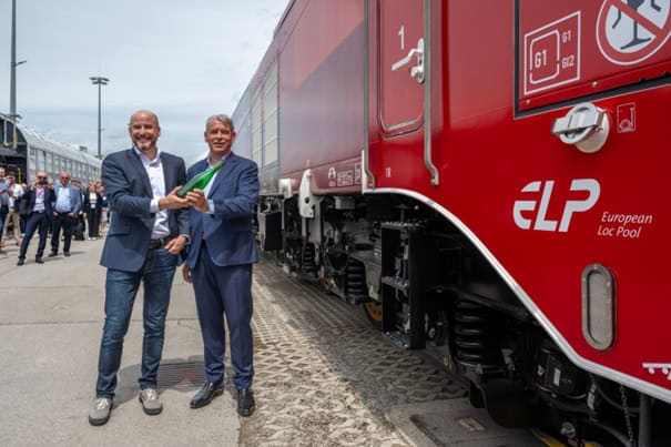 Two men shaking hands near red train.